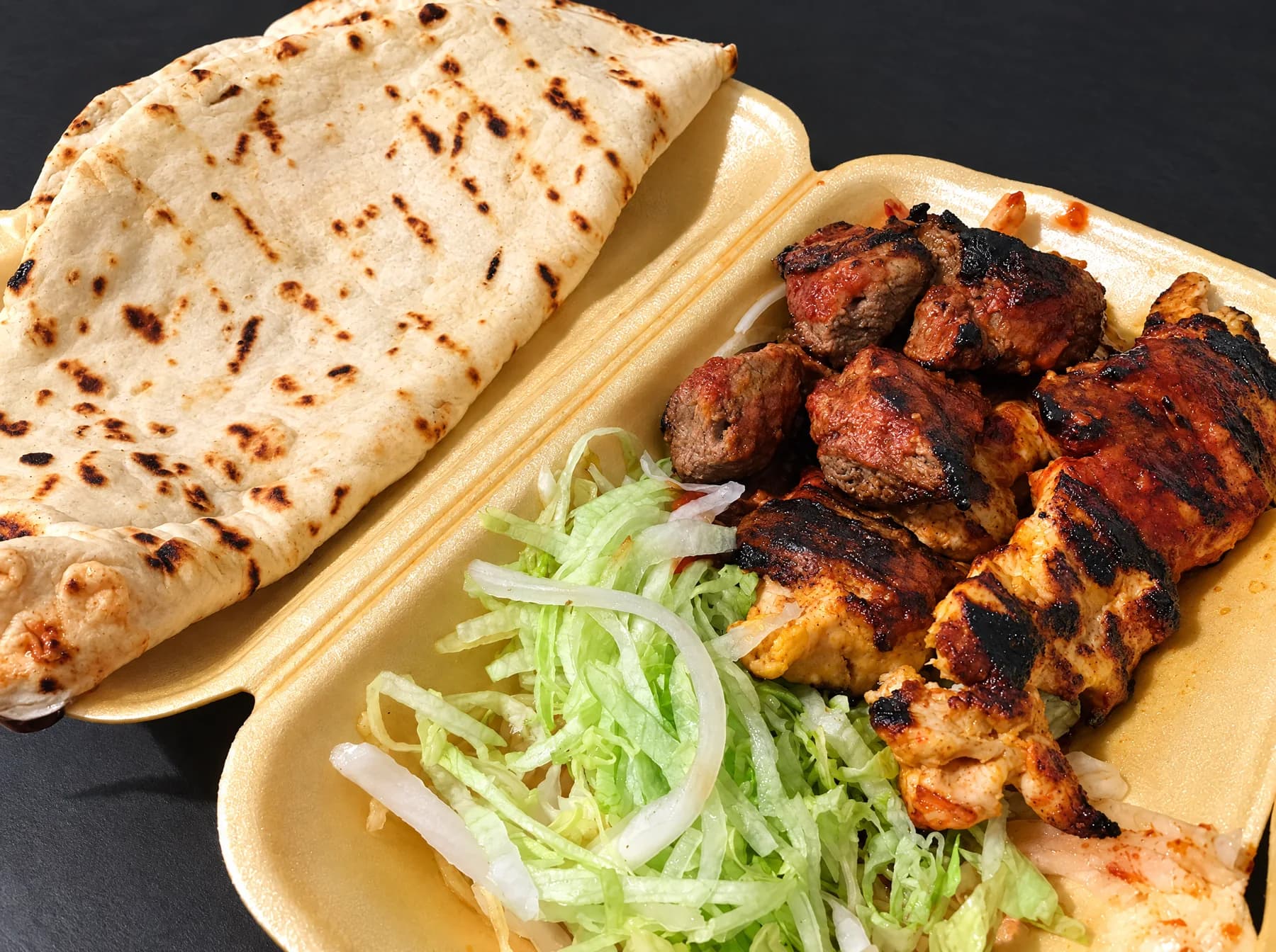 Chargrilled lamb and chicken with shredded salad and naan bread in a takeaway box