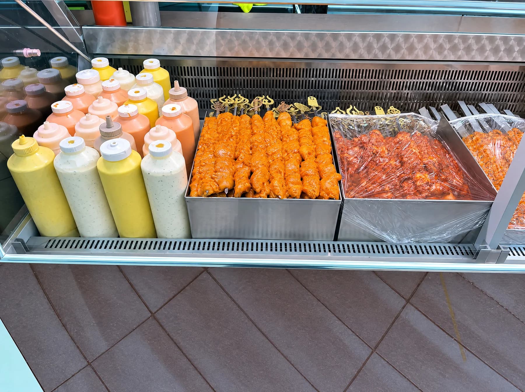 Rows of sauce bottles and trays of marinated meat behind the counter glass